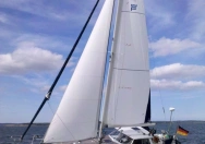 Ein Segelboot mit weißen Segeln von Rolly Tasker Sails nutzt den Wind und fährt sportlich mit reichlich Krängung bei Sonnenschein auf offener See.