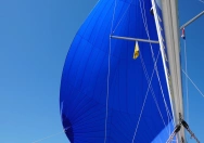 Segelboot mit einem leuchtend blauen Spinnaker, der sich im Wind entfaltet, unter klarem Himmel auf offener See.