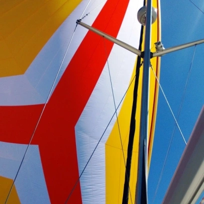 Zu sehen ist ein individuell gestalteter gehisster Spinnaker von Sailselect in den leuchtenden Farben gelb, rot und weiß.